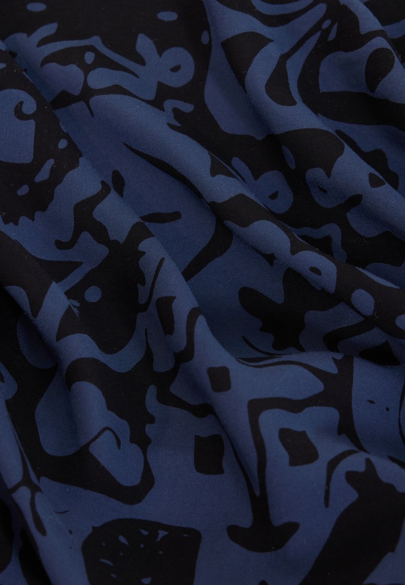 Dunkelblauer Stoff mit unregelmäßigen schwarzen abstrakten Formen und Mustern, gezeigt mit natürlichen Falten und Schatten.