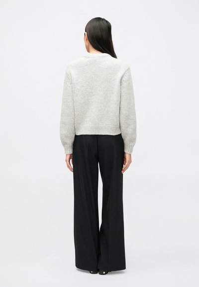 Svetlosivý pletený sveter s okrúhlym výstrihom a rebrovaným lemom, v kombinácii s čiernymi širokými nohavicami s prúžkovaným vzorom.
