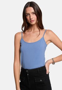 Débardeur bleu clair à fines bretelles, présentant une texture lisse et un design ajusté. Associé à un pantalon noir taille haute.