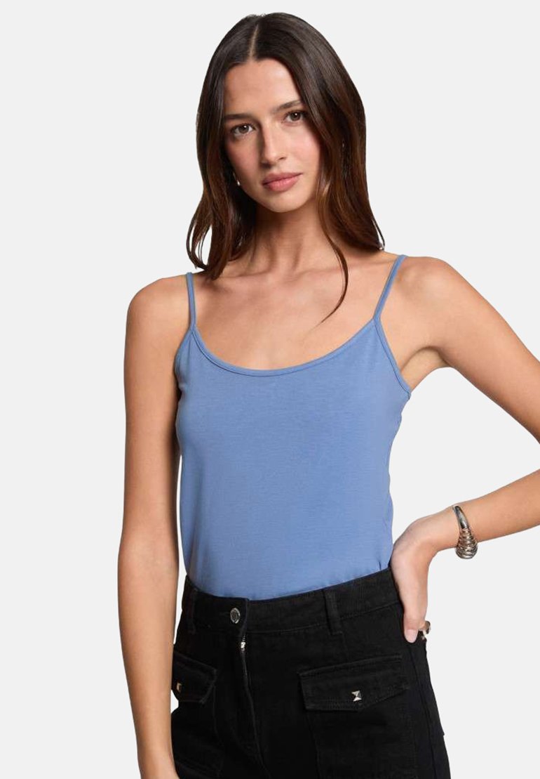 Débardeur bleu clair à fines bretelles, présentant une texture lisse et un design ajusté. Associé à un pantalon noir taille haute.