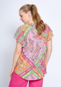 Bunte Bluse mit Paisley-Muster in Pink, Orange und Grün, mit kurzen Rüschenärmeln. Leichter Stoff mit lässiger Passform und abgerundetem Saum.