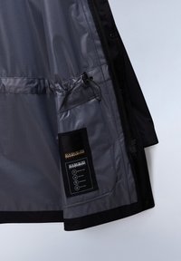 Svart och grå jacka med en glänsande insida, som har en snoddknäppning och ett märke med skötselråd och varumärkesinformation.