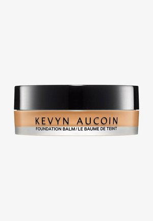 Baume de la Fondation Kevyn Aucoin dans un pot rond et transparent avec un couvercle noir. Le produit a une teinte crémeuse beige avec une texture lisse.