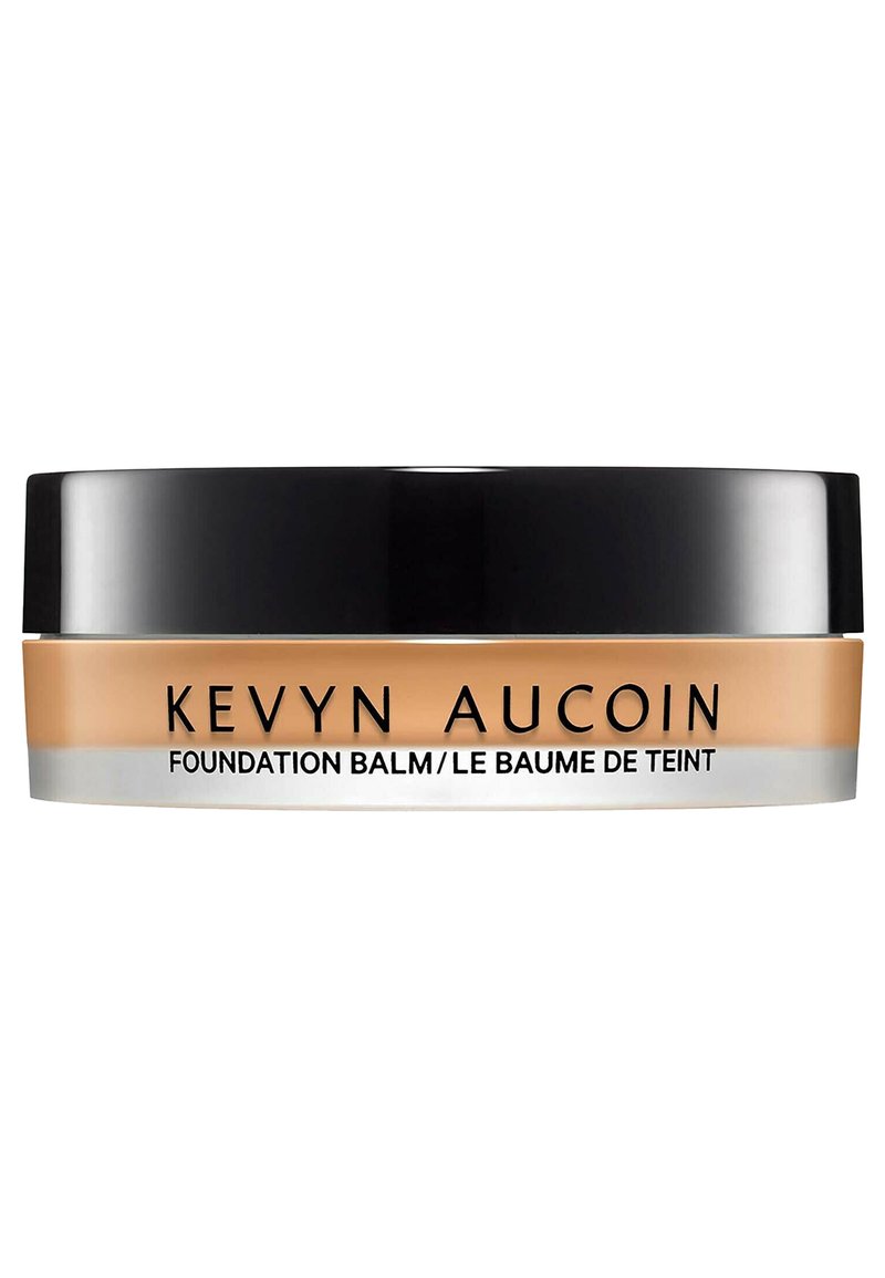 Baume de la Fondation Kevyn Aucoin dans un pot rond et transparent avec un couvercle noir. Le produit a une teinte crémeuse beige avec une texture lisse.