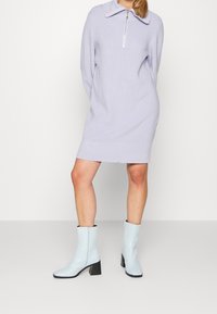 Abito maglione a costine lilla con colletto a zip, abbinato a stivaletti alla caviglia azzurro cielo con tacco a blocco e dettagli con zip.