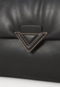Svart lærveske med teksturert overflate og en gullbelagt trekantet låsdetalj. Glatt, strømlinjeformet design med en minimalistisk estetikk.
