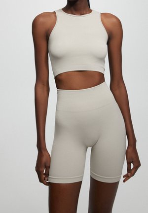 Femme portant un crop top en ribbed beige et un short de cycliste taille haute, se tenant contre un fond clair et uni.