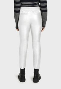 Witte, gladde broek met een slim fit, elastische tailleband en twee achterzakken; gedragen met zwarte chunky laarzen en een grijs gestreept sweater.