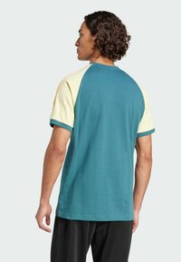 Short-sleeve t-shirt featuring a teal body with yellow and orange raglan sleeves, made of soft cotton fabric, with a round neckline.