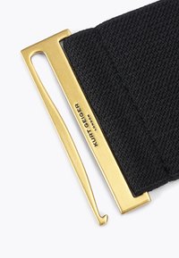 Czarny pleciony pasek materiałowy z złotą klamrą w kształcie haka, na której wygrawerowane jest "Kurt Geiger London", na białym tle.