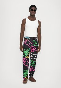 Black denim pants with colorful abstract patterns in pink, green, yellow, and white; paired with a white tank top and brown shoes.