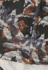 Textiel met een zwart, wit en roestkleurig patroon. Bevat abstracte vormen in paars, oranje en grijs, met een geweven textuur en label.