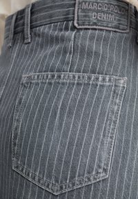 Grå denim jeans med hvite vertikale striper, med en baklomme og en merket lærpatch på livet.