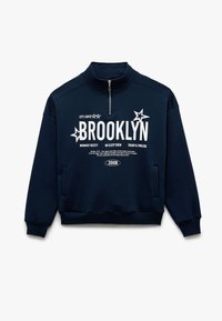 Sudadera azul marino con cuello alto, cremallera de cuarto y texto impreso en blanco. Con estrellas y un bolsillo tipo canguro. Textura de tela suave.
