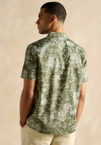 Tričko s krátkym rukávom olivovej farby s bielou námornou a tropickou potlačou. Má klasický golier a voľný strih, sieťovú textúru.