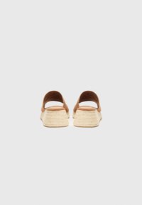 Ruskean mokkanahkasaappaat, joissa on leveä hihna ja teksturoitu vaaleanbeige espadrille-korko. Korko on pyramidin muotoinen ja siinä on punottu kuvio.