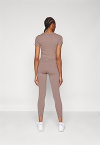 Brown fitted crop top and leggings made of stretchy fabric, accented by a small logo on the back. Worn with white athletic shoes.