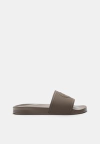 Sandale en caoutchouc texturé de couleur marron. Elle présente une large sangle avec un logo circulaire, une semelle plate et un design minimaliste.