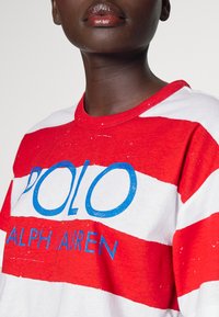 Röd och vitrandig t-shirt med en blå "POLO"-logotyp och texten "RALPH LAUREN", med rund halsringning och mjukt, texturerat tyg.