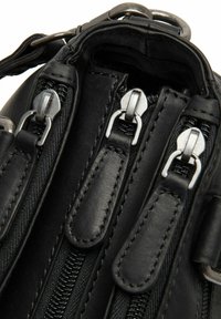 Zwarte leren tas met meerdere zilveren ritsen, een gestructureerd oppervlak en stevige stiksels. Inclusief metalen hardware en stoffen accenten.