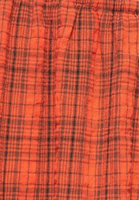 Tissu orange avec un motif à carreaux noirs comportant des lignes horizontales et verticales, et une couture élastique froncée sur le bord supérieur.