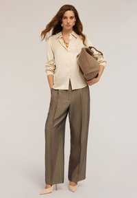 Beige satijnen overhemd met knopen, geplooide groene gestreepte wijde broek, neutrale tas met handvat, en lichte pumps. Soepele texturen en een nauwsluitende pasvorm.
