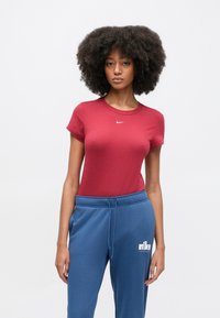 Ερυθρό στενό T-shirt με στρογγυλή λαιμόκοψη και κοντά μανίκια, διακοσμημένο με μικρό λευκό λογότυπο της Nike. Συνοδεύεται από μπλε φόρμες. Μαλακή υφή.