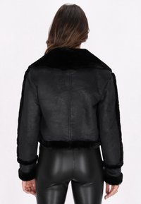 Schwarze, kurz geschnittene Jacke aus Kunstfell mit einer weichen, glänzenden Textur, großem Kragen und taillierten Ärmeln, kombiniert mit schwarzen, hochgeschnittenen Leggings.