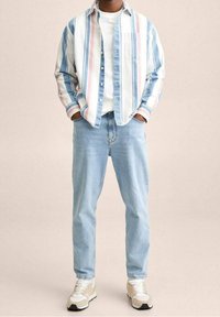 Koszula w paski w kolorach niebieskim, białym i różowym, noszona na białym t-shircie; zestawiona z jasnoniebieskimi dżinsami i beżowymi trampkami.