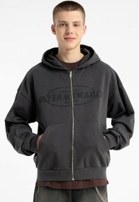 Szara bluza z kapturem, z zapięciem z przodu, dużymi kieszeniami z przodu oraz nadrukiem "INFLAMMABLE" na czarnym tle. Miękki, luźny krój.