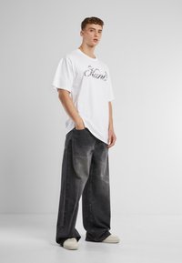 White cotton oversized t-shirt with "Hand" print, paired with dark gray denim wide-leg jeans, featuring subtle textures and white sneakers.
