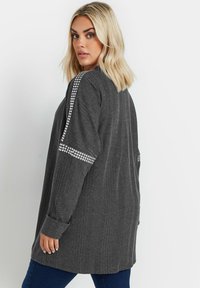 Grå texturerad långärmad topp med lös passform, med glänsande detaljer längs axlarna och knäppte manschettdetaljer.