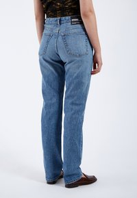 Vaqueros de mezclilla azul claro con un diseño de pierna recta, que cuentan con una cintura alta, bolsillos traseros y una etiqueta de marca en la cinturilla.