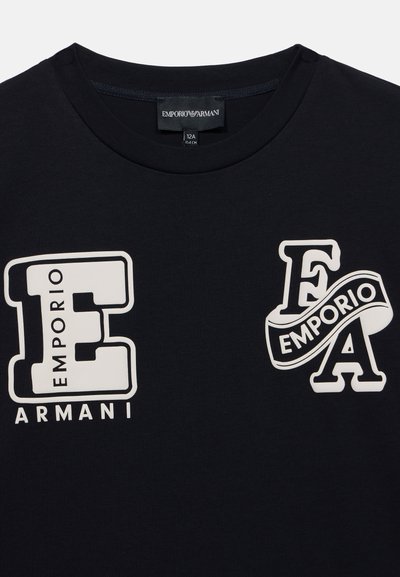 Μαύρο πουκάμισο με ετικέτες Emporio Armani, με μεγάλα λευκά γράμματα E και FA με τις λέξεις Emporio και Armani στο μπροστινό μέρος.