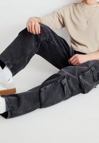 Svarta cargobyxor med avslappnad passform, har flera fickor och en blekt denimtextur. Bärs med en beige topp och grå skor.