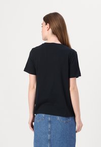 T-shirt nera a maniche corte con collo rotondo, realizzata in cotone, mostrata di spalle. Abbinata a una gonna di jeans chiara.