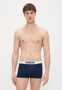 Tumši zili bokseršorti no elastīga auduma ar baltu elastīgu jostiņu, uz kuras redzams "DIESEL" logotips. Pielāgota piegriezuma ar minimālām šuvēm.