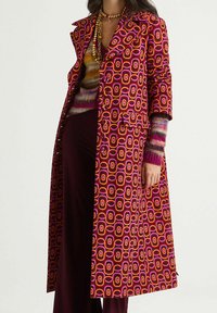 Cappotto lungo con motivo geometrico vivace in rosa, arancione e viola. Ha un design su misura con colletto e tasche laterali.