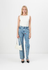 Lichtgewicht witte geribbelde tanktop, blauwe denim jeans met geborduurde patronen, witte handtas met veters en zwarte puntige hakken.