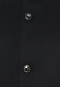 Primer plano de tela negra con dos botones oscuros brillantes asegurados por hilo negro en alineación vertical.