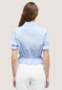 Blue short-sleeve shirt with floral white embroidery, collared design, elastic waistband, and ruffled hem. Smooth fabric texture.