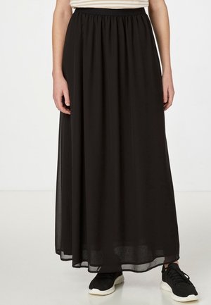 Mujer con una falda larga, negra y fluida con una cintura elástica, combinada con zapatillas negras y blancas.