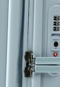 Valigia blu chiaro con una finitura testurizzata, dotata di due cerniere argento, una serratura a combinazione e un piccolo emblema. Dettagli di cucitura chiari visibili.