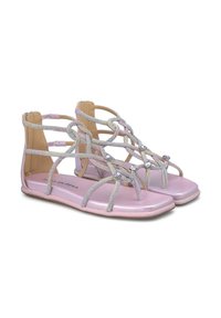 Sandalias planas rosas con un brillo metálico, diseñadas con correas decorativas y pequeñas gemas. Presentan un respaldo abierto y una suela texturizada.