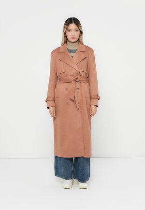 Lang trenchcoat i myk rosa stoff, med dobbeltknappede knapper, bred krage, belte og knytning i livet. Kombinert med vide jeans.