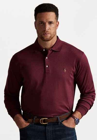 Burgunderfarget langermet polo skjorte med en tre-knaps placket og et brodert logo på brystet. Kombinert med denim og et brunt belte.