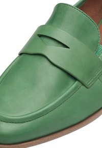 Grüne Lederloafers mit einem breiten Riemen und Aussparung, runder Zehenpartie und brauner Gummisohle. Glatte Textur und schlichtes Design.