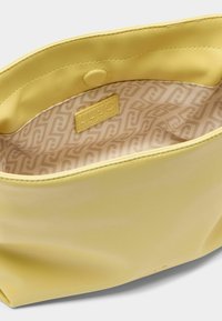 Sac en cuir jaune avec une texture lisse, doté d'une fermeture à pression et d'une doublure en tissu à motifs avec une étiquette logo à l'intérieur.