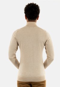 Maglione beige a collo alto con maniche lunghe, texture liscia, polsini e orlo a costine, e dettagli di cucitura sottili sulle spalle.