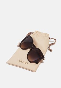 Tortoiseshell sunglasses with large, angular frames sit on a beige drawstring pouch, featuring the embossed logo "LIUJO" in gold.